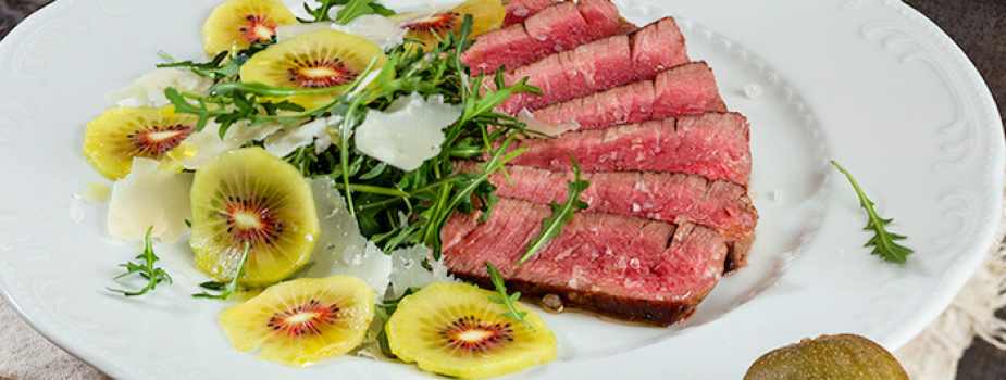 Carne de vacuno en rodajas con rúcula, kiwi y pétalos de parmesano