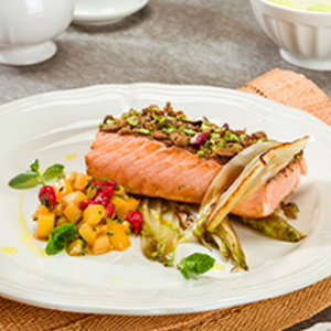 Lachs in Vollkornbrot-Pistazien-Kruste auf einem Bett aus gebratenem Chicorée mit würfelig geschnittener Kiwi, Johannisbeeren und Minze